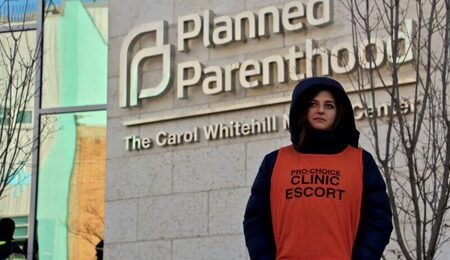A_clinic_escort_outside_the_Planned_Parenthood_-_Carol_Whitehill_Moses_Center_38949360565-1-e1660827220849.jpg